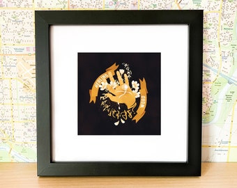 May include: A black framed print with a gold design of a hand with flowers and the words "Healing Word" on a black background.