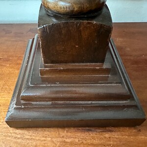 May include: A dark brown wooden lamp base with a square top and a rounded column. The base has a layered design with multiple tiers.