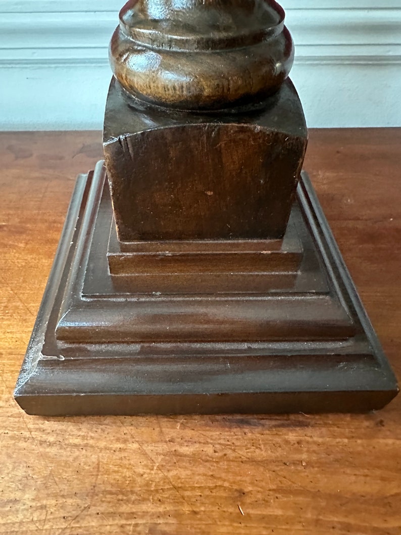May include: A dark brown wooden lamp base with a square top and a rounded column. The base has a layered design with multiple tiers.
