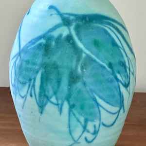 May include: A light blue ceramic vase with a unique abstract design in shades of blue and green.