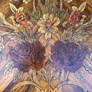 May include: Intricate marquetry design featuring a floral motif with roses, leaves, and vines. The design is crafted from various wood veneers in shades of brown, gold, and purple.
