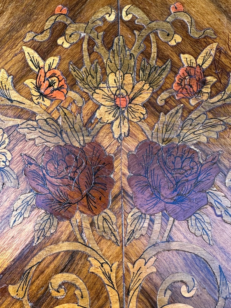 May include: Intricate marquetry design featuring a floral motif with roses, leaves, and vines. The design is crafted from various wood veneers in shades of brown, gold, and purple.