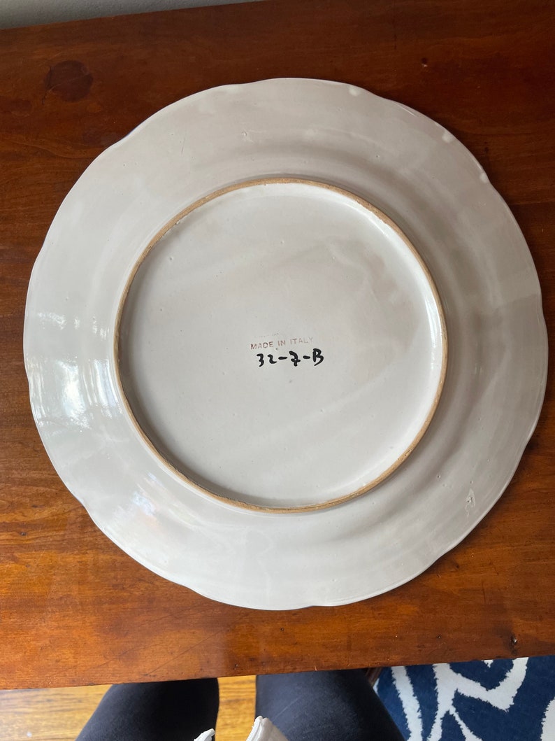 K&ouml;nnte beinhalten: Ein wei&szlig;er Keramikteller mit einem gewellten Rand und einem braunen Rand. Auf der R&uuml;ckseite des Tellers steht in schwarzer Schrift "Made in Italy" und "31-7-B".
