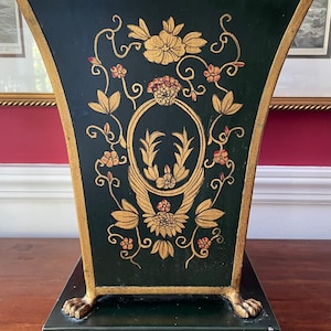 May include: A black and gold decorative planter with a floral design. The planter has a square base and a wide, flared top. The floral design is painted in gold and red on a black background.