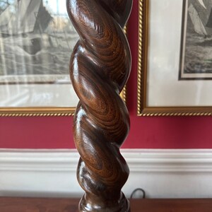 May include: A dark brown wooden lamp base with a twisted, spiral design. The base is made of a single piece of wood and has a square base.