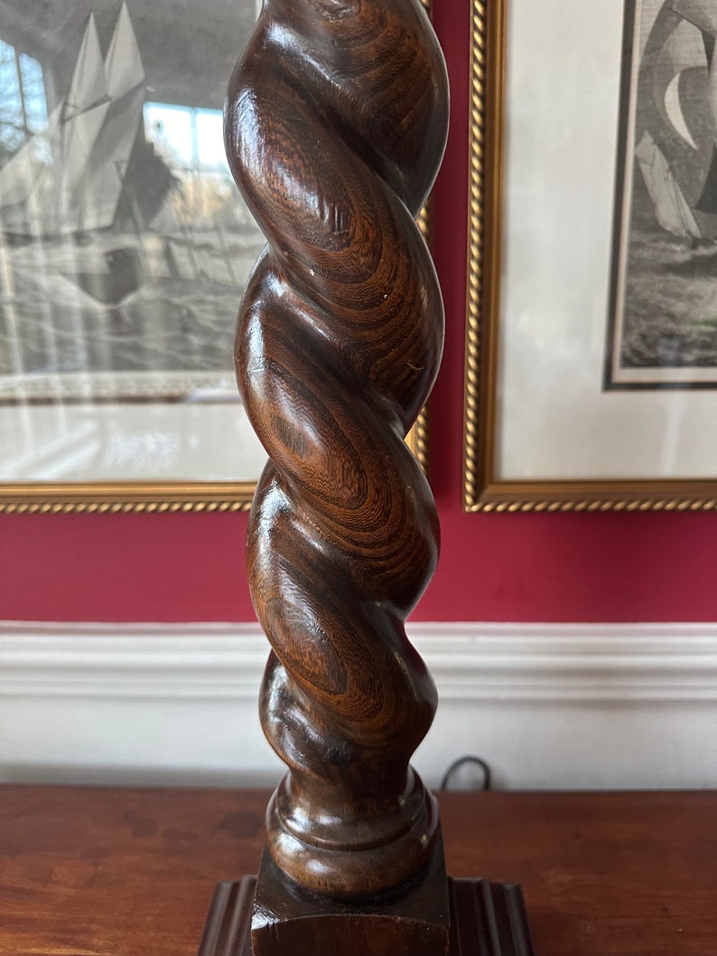 May include: A dark brown wooden lamp base with a twisted, spiral design. The base is made of a single piece of wood and has a square base.