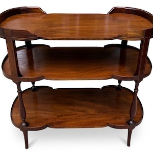 May include: A three-tiered wooden stand featuring a rich brown finish and a smooth, polished surface. Each of the three shelves has a distinct, curved, scalloped edge design, supported by four slender, turned wooden legs that connect the levels.