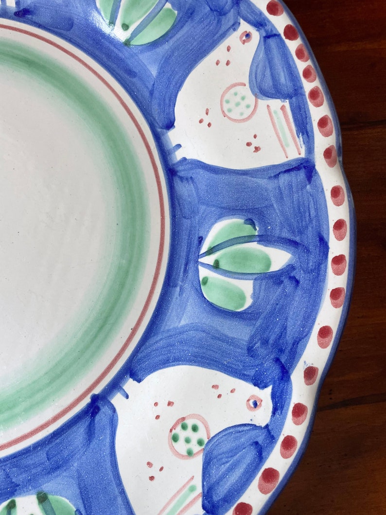 K&ouml;nnte beinhalten: Ein wei&szlig;er Keramikteller mit blauem Rand und einem gr&uuml;n-blauen Design. Das Design zeigt stilisierte V&ouml;gel und Bl&auml;tter.