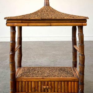 May include: A small, brown bamboo table with a thatched roof top and a drawer. The table has a woven bamboo top and bottom shelf.