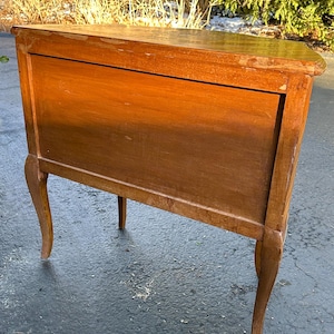 May include: A wooden corner cabinet with a light brown finish. The cabinet has a single door and sits on four legs with a curved design.