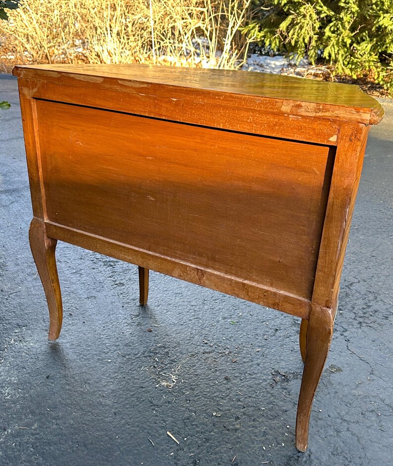 May include: A wooden corner cabinet with a light brown finish. The cabinet has a single door and sits on four legs with a curved design.
