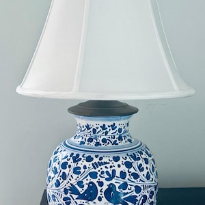 May include: A ceramic table lamp with a white lampshade. The base is a blue and white vase with a floral and bird design. The lamp is on a dark wooden surface.