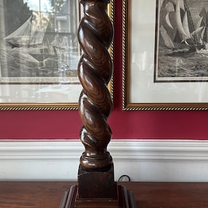 May include: A dark brown wooden table lamp with a twisted column and a square base. The lamp has a gold metal shade holder and a gold metal cord.