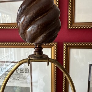 May include: A gold lamp base with a brown wooden finial. The finial is shaped like a swirl or a knot.