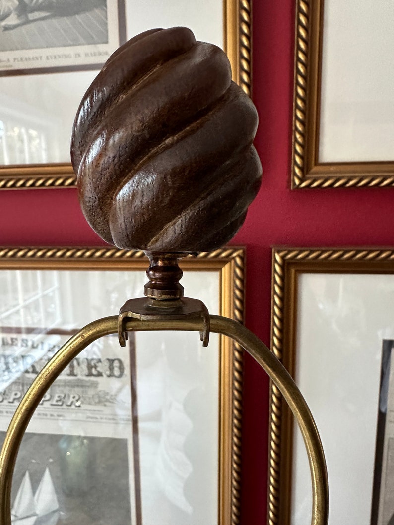 May include: A gold lamp base with a brown wooden finial. The finial is shaped like a swirl or a knot.