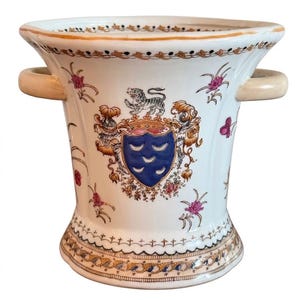 May include: A white ceramic vessel with two side handles, featuring a central blue shield crest with three crescent moons, topped by a small tiger figure. The exterior is decorated with hand-painted floral motifs and gold-toned trim borders.