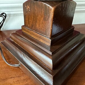 May include: A dark brown wooden lamp base with a tiered design. The base has a rounded top and a square bottom. The base is made of solid wood and has a smooth finish.