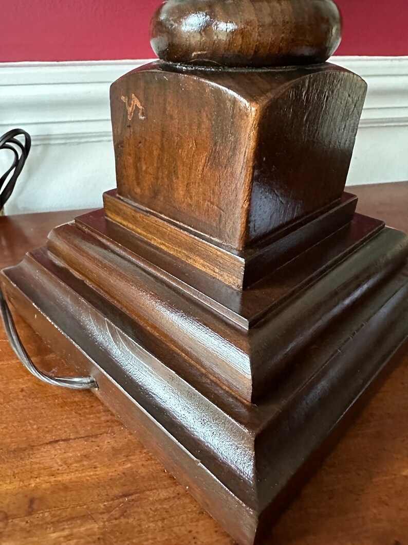 May include: A dark brown wooden lamp base with a tiered design. The base has a rounded top and a square bottom. The base is made of solid wood and has a smooth finish.