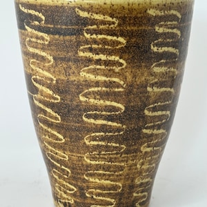 May include: A tall, yellow ceramic vase with a brown, abstract pattern. The vase has a wide mouth and a narrow base.
