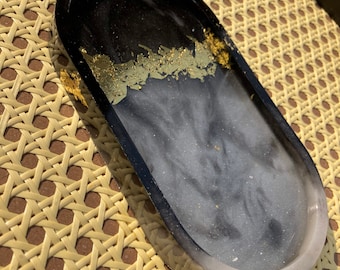 May include: Black and white oval tray with gold leaf accents. The tray is made of resin and has a glossy finish.