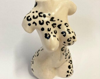 May include: A ceramic sculpture of a female torso with a black and white leopard print design.