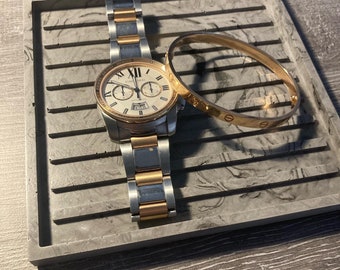 May include: A gold and silver watch with a white face and a gold bracelet. The watch is on a gray marble tray with a gold bangle bracelet.
