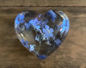May include: A heart-shaped resin paperweight with blue forget-me-not flowers pressed inside.