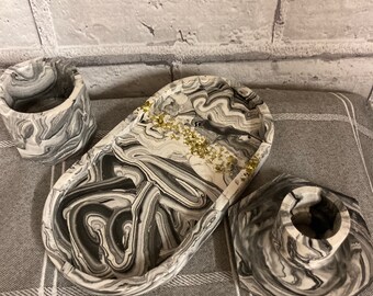 May include: Three decorative trays with a black and white marbled design. The trays are made of resin and have a glossy finish. The largest tray is oval shaped and the two smaller trays are round. The trays are perfect for holding jewelry, keys, or other small items.