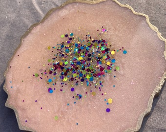 May include: A pink resin coaster with a gold edge and a scattering of colorful glitter in the center.