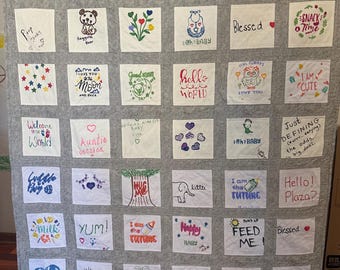 May include: A handmade grey quilt with many embroidered squares. Each square has unique text and illustrations, including phrases like "Favorite Child," "Hello World," and "I am the Future." The quilt is personalised with a name at the bottom.
