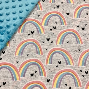 Puede incluir: Una manta para beb&eacute; con tela de lunares minky azul claro y una tela gris estampada con arco&iacute;ris pastel y corazones negros. Los arco&iacute;ris tienen arcos rosas, amarillos, azules y morados. La manta es suave.