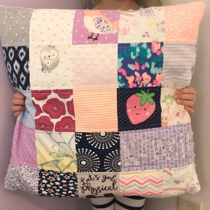 May include: A patchwork pillow with a variety of fabric squares. The squares feature patterns like floral, geometric, and animal prints, including a bird, owl, and strawberry. The phrase "Let's get Physical" is embroidered on one square. The pillow is held by a person.