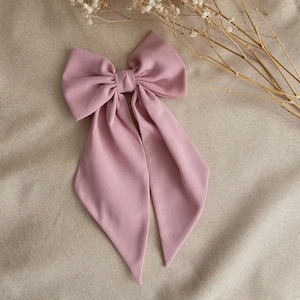 Puede incluir: Un gran lazo rosa polvoriento con colas largas. El lazo está hecho de tela y tiene un diseño simple y elegante.