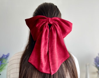 May include: A large, burgundy satin bow hair tie. The bow is tied in a large, loose knot and the tails are long and flowing.