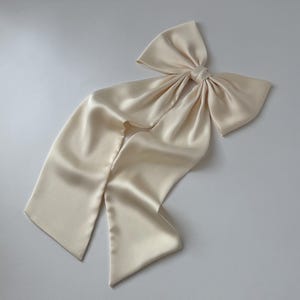 May include: A large, ivory satin bow with long tails. The bow is tied in a knot and the tails are flowing.