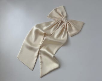 May include: A large, ivory satin bow with long tails. The bow is tied in a knot and the tails are flowing.