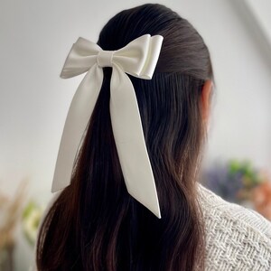 Puede incluir: Un lazo de sat&eacute;n blanco con colas largas, atado en el cabello de una persona.