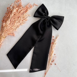 Könnte beinhalten: Eine große schwarze Schleife aus Satin mit langen Bändern. Die Schleife ist zu einem Knoten gebunden und die Bänder fallen herab.
