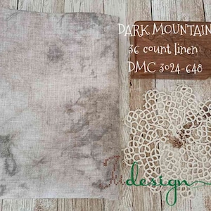 May include: A piece of gray linen fabric with a mottled pattern, next to a wooden box with the text "DARK MOUNTAIN 36 count linen DMC 3024-648". A white lace doily is also present. The items are arranged on a wooden surface.