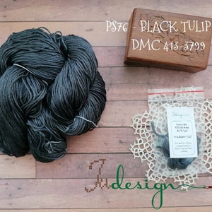 Könnte beinhalten: Eine Spule schwarzen Seidenfadens mit der Aufschrift "PS76 - BLACK TULIP silk DMC 413-3799" und eine kleine Tüte schwarzen Fadens mit einem Etikett, auf dem "BLACK TULIP" steht.