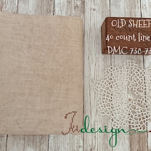 Könnte beinhalten: Ein Stück beigefarbenes Leinengewebe mit einem Holzblock, auf dem "OLD SHEEP 40 count linen DMC 738-739" steht, und einer weißen Häkelspitze.