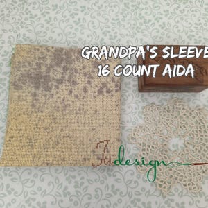 May include: A cross-stitch project with the text "GRANDPA'S SLEEVE 16 COUNT AIDA". The image includes a piece of beige Aida cloth with a faded gray design, a small wooden box, and a cream-colored doily.