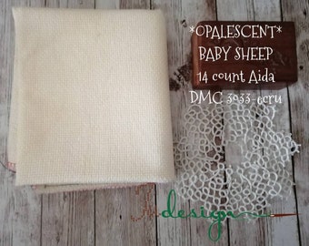 Peut inclure: Un tissu Aida blanc avec un bloc en bois qui dit "*OPALESCENT* BABY SHEEP 14 count Aida DMC 3033 - ecru" et une dentelle blanche.