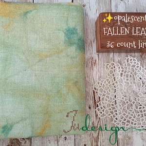 May include: A piece of 36 count linen fabric dyed in shades of green and yellow. The fabric is labeled "Opalescent Fallen Leaves 36 count linen".