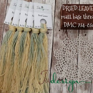 May include: Five skeins of DMC embroidery floss in shades of yellow and green. The floss is labeled "Dried Leaves" and the DMC color numbers are 734-834. The floss is displayed on a wooden surface with a white lace doily.