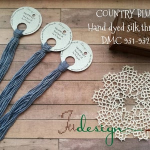 May include: Three skeins of hand-dyed silk thread in a blue shade called "Country Blue". The thread is wound around cardboard circles with the name and DMC colour numbers 931-932. A white lace doily is also pictured.