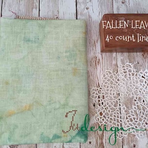 May include: A piece of green linen fabric with a light brown border. The fabric is labeled "FALLEN LEAVES 40 count linen".