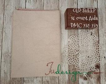 Peut inclure: Un tissu beige Aida avec une bordure rose, prêt pour le point de croix. Le texte "OLD SHEEP 16 count Aida DMC 738-739" est imprimé sur un bloc de bois.