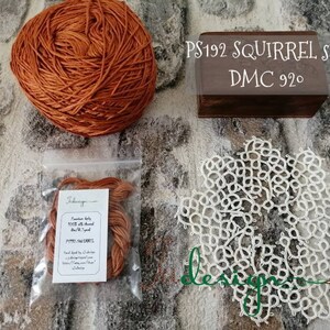 May include: A skein of orange silk thread labelled "PS192 SQUIRREL silk DMC 920" with a small bag of the same thread and a white crocheted doily.