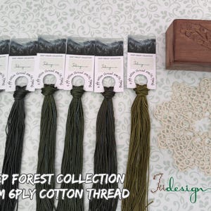 May include: A collection of six skeins of Deep Forest Collection 6x8M 6-ply cotton thread in various shades of green, with a wooden box and a cream-colored doily. The thread colors range from light to dark green.